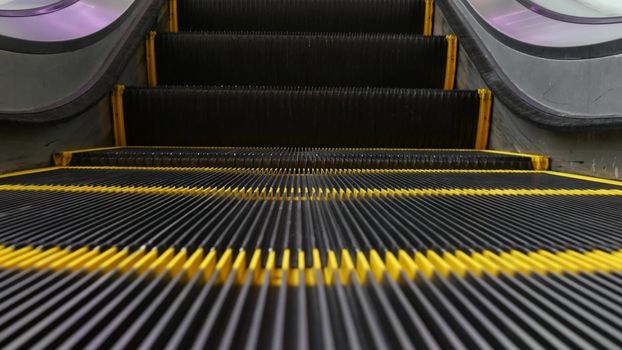 Low angle looped perspective view of modern escalator stairs. Automated elevator mechanism. Yellow line on stairway illuminated with purple light. Futuristic empty machinery staircase moving straight.