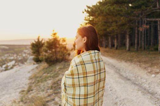 A woman on the road near the forest looks to the side and a plaid on her shoulders. High quality photo