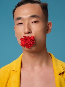 The guy is Korean appearance with a flower in his mouth on a blue background and a yellow jacket. High quality photo