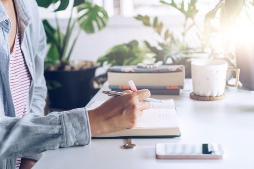 Woman is writing in planner notebook while using laptop to work or plan with workspace at home. Education business lifestyle concept.