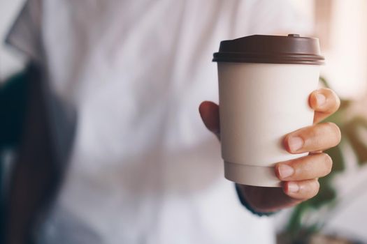 Hand hold a cup of coffee with sunlight flare beautiful copy space background. Wake up caffeine intake in morning time.