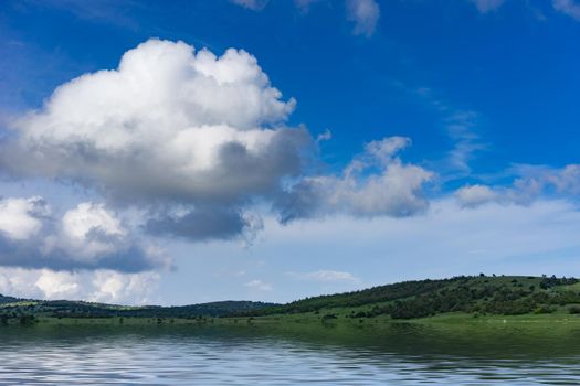 Natural landscape with a green field covered with grass under the blue sky with clouds.