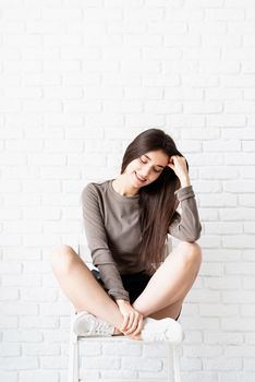 beautiful brunette woman with long hair wearing brown shirt and black leather shorts sitting on the chair, thinking and smiling