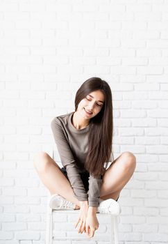 beautiful brunette woman with long hair wearing brown shirt and black leather shorts sitting on the chair, thinking and smiling