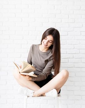 Woman in brown shirt sitting on the chair with legs crossed holding an opened book