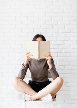 Woman in brown shirt sitting on the chair with legs crossed holding an opened book