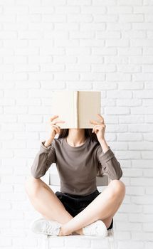 Woman in brown shirt sitting on the chair with legs crossed holding an opened book