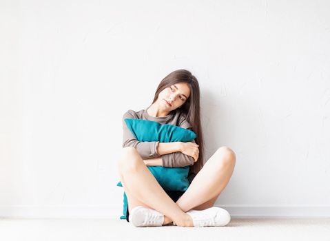 Mental health concept. Beautiful sad woman in brown shirt and black leather shorts sitting on the floor with pillow deep in thought