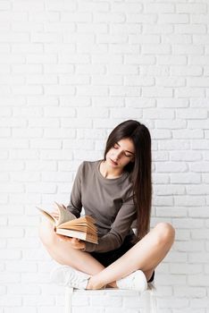 Woman in brown shirt sitting on the chair with legs crossed holding an opened book