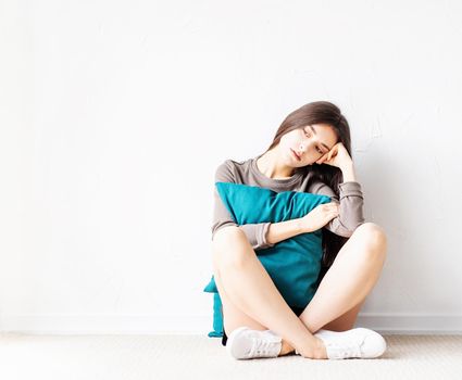 Mental health concept. Beautiful sad woman in brown shirt and black leather shorts sitting on the floor with pillow deep in thought