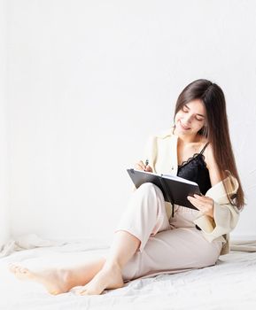 Beautiful sexy woman in comfy home clothes writing notes sitting on the floor, thinking