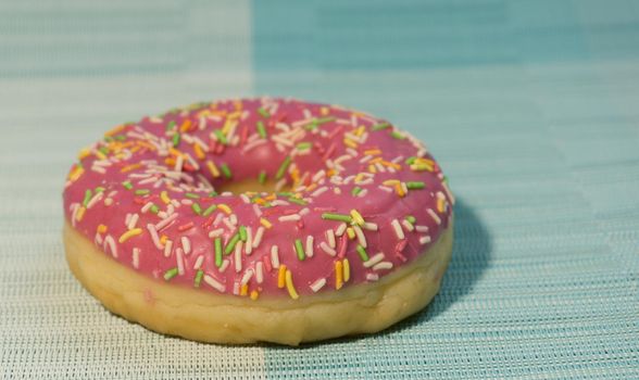 Pink sweet doughnut or donut with colored sprinkles on a blue background. Bitten off American bagel.