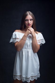 Portrait of a beautiful girl in a loose white dress on a black background