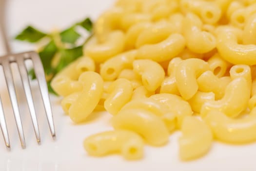 Boiled yellow pasta on a white plate with a fork. Close-up.