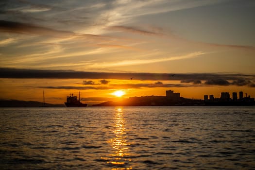 Seascape with a view of the silhouette of the city and the ship on the background of the sunset. Vladivostok, Russia