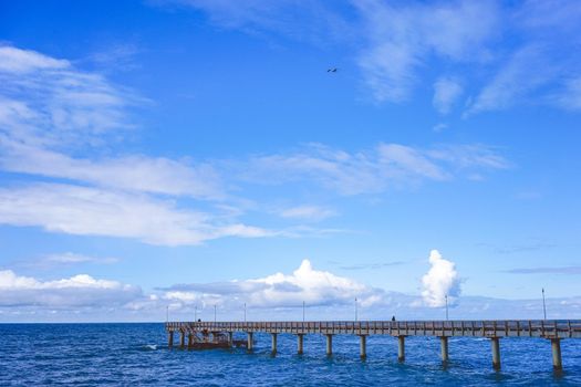 Seascape overlooking the long pier of the resort town with walking people.