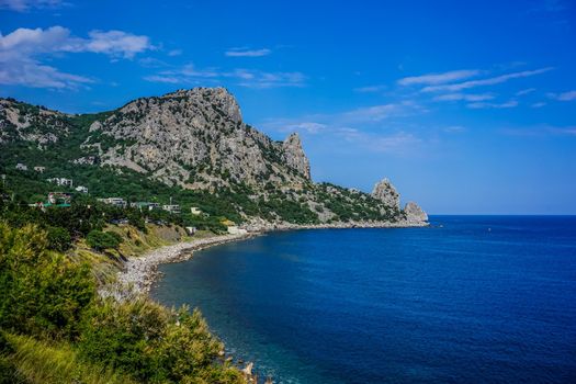 Rock covered with green vegetation hanging over the calm blue sea in a bright summer day