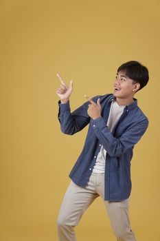 portrait of happy handsome young asian man dressed casually pointing fingers at copyspace isolated on yellow studio background