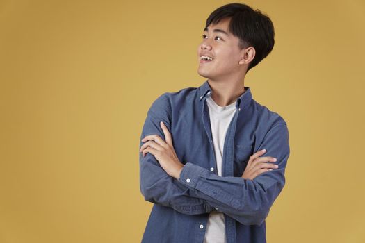 portrait of happy handsome young asian man dressed casually with folded crossed arms gesture isolated on yellow studio background