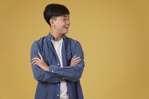 portrait of happy handsome young asian man dressed casually with folded crossed arms gesture isolated on yellow studio background