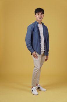 portrait of smiling happy cheerful young asian man dressed casually isolated on yellow studio background