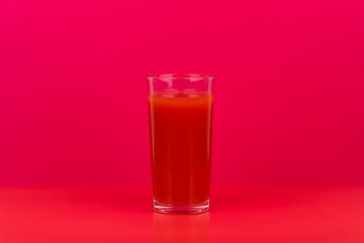 Glass of tomato juice on red table against pink background with copy space. Concept of vegetarian lifestyle, fresh juices, healthy food and wellness