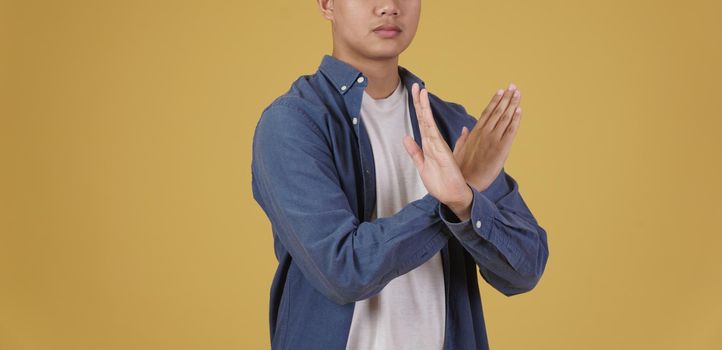 portrait of handsome young asian man dressed casually crossing arms in negative rejection or no expression isolated on yellow studio background