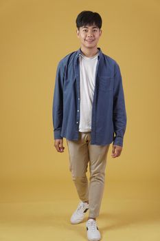 portrait of handsome young asian man dressed casually isolated smiling walking on yellow studio background