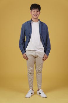 portrait of cheerful happy rejoicing young asian man dressed casually smiling isolated on yellow studio background