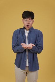 portrait of surprised excited young asian man dressed casually holding something on open palms isolated on yellow studio background