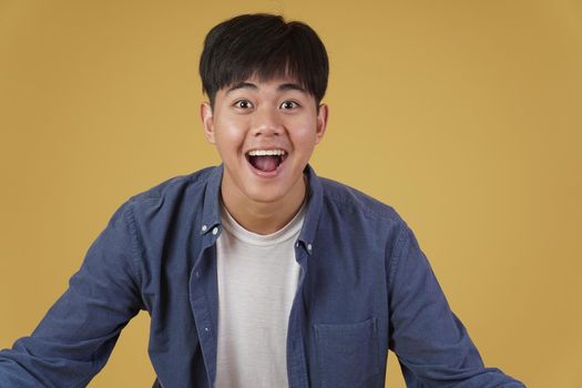 portrait of  glad cheerful happy rejoicing excited overjoyed young asian man dressed casually isolated on yellow studio background