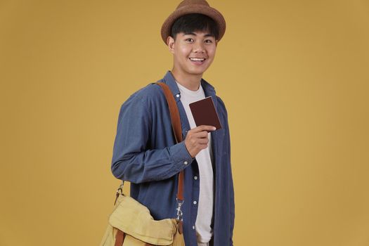 young asian man traveler smiling holding passport isolated on yellow background. Travel journey trip in holiday vacation