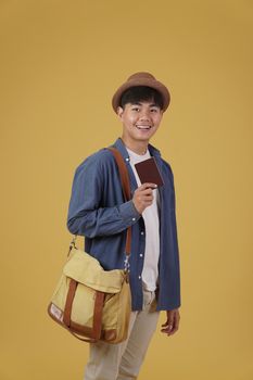 young asian man traveler smiling holding passport isolated on yellow background. Travel journey trip in holiday vacation