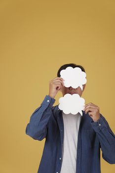 portrait of smiling happy cheerful young asian man dressed casually with empty speech bubble isolated on yellow studio background