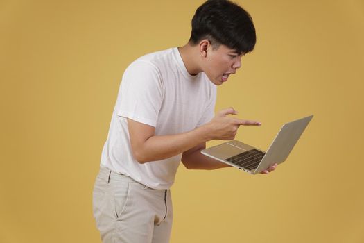aggressive angry upset furious young asian man scolding screaming yelling on laptop computer isolated on yellow studio background