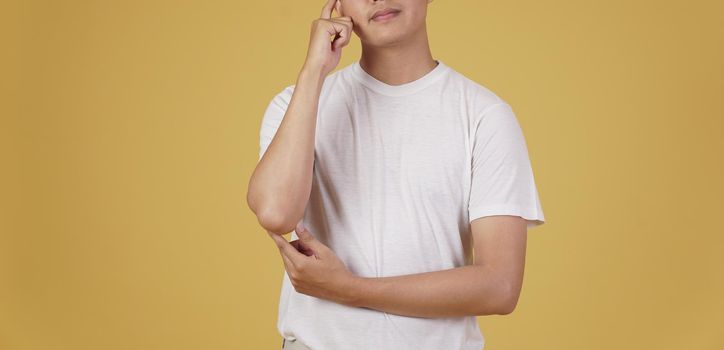 portrait of thoughtful young asian man dressed casually thinking doubting wondering isolated on yellow studio background