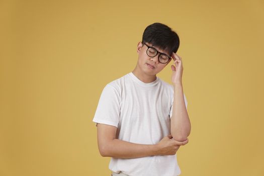 portrait of thoughtful young asian man dressed casually thinking doubting wondering isolated on yellow studio background