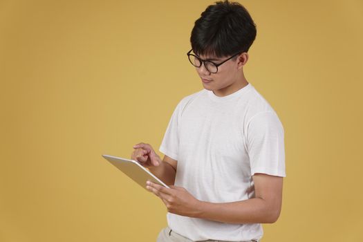 young asian man dressed casually using digital tablet isolated on yellow studio background.