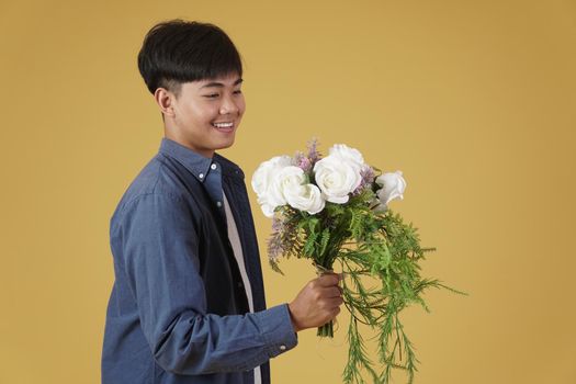smiling happy cheerful young asian man dressed casually holding flower bouquet isolated on yellow studio background.