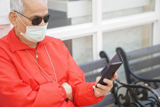 asian old elder senior man elderly male wearing face mask using mobile smart phone cellphone outdoor. mature retirement lifestyle