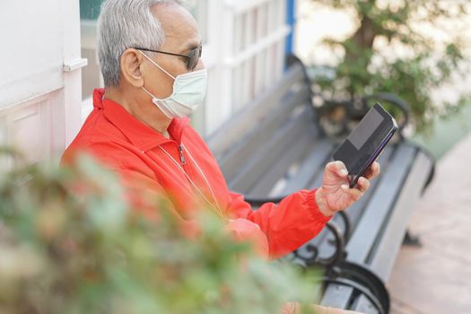 asian old elder senior man elderly male wearing face mask using mobile smart phone cellphone outdoor. mature retirement lifestyle