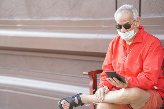 asian old elder senior man elderly male wearing face mask using mobile smart phone cellphone outdoor. mature retirement lifestyle