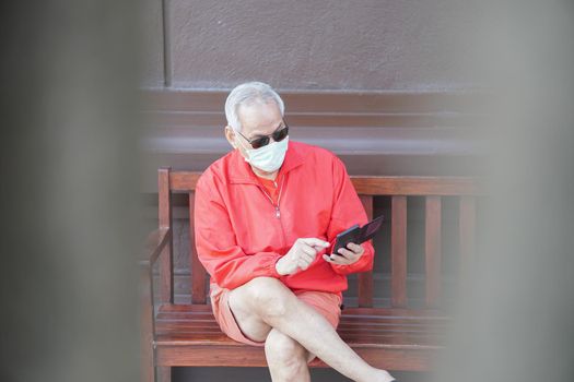 asian old elder senior man elderly male wearing face mask using mobile smart phone cellphone outdoor. mature retirement lifestyle