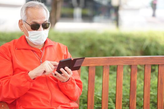 asian old elder senior man elderly male wearing face mask using mobile smart phone cellphone outdoor. mature retirement lifestyle