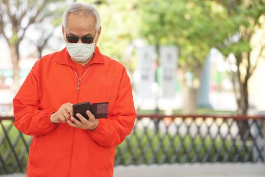 asian old elder senior man elderly male wearing face mask using mobile smart phone cellphone outdoor. mature retirement lifestyle