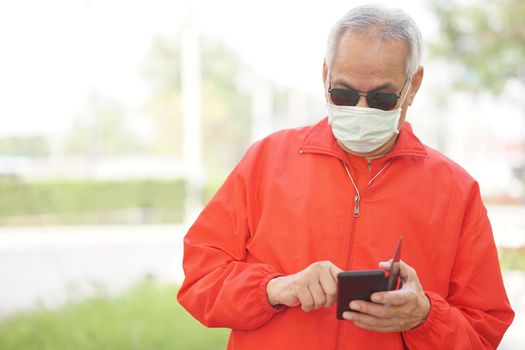 asian old elder senior man elderly male wearing face mask using mobile smart phone cellphone outdoor. mature retirement lifestyle