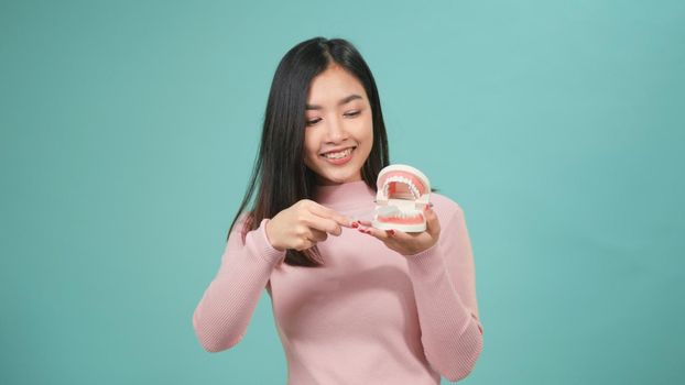 Asian young beautiful woman smile showing model how to clean the teeth with toothbrush properly and right, Female brush white teeth model isolated on blue background, dental hygiene and health concept