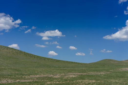 Natural landscape with hills against blue sky with white clouds.