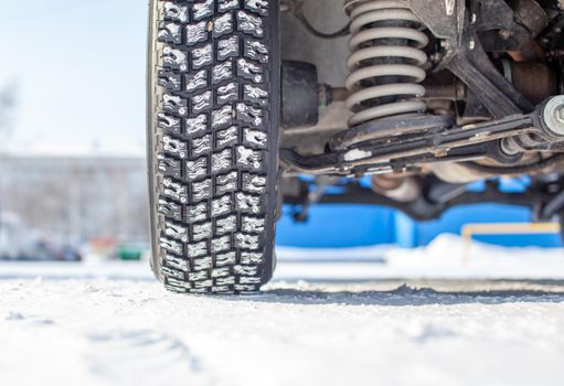 Car wheel on snow in winter close-up. The suspension and chassis of the car are visible. The car is parked in a snowy parking lot.