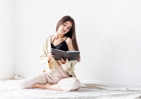 Beautiful sexy woman in comfy home clothes writing notes sitting on the floor, thinking